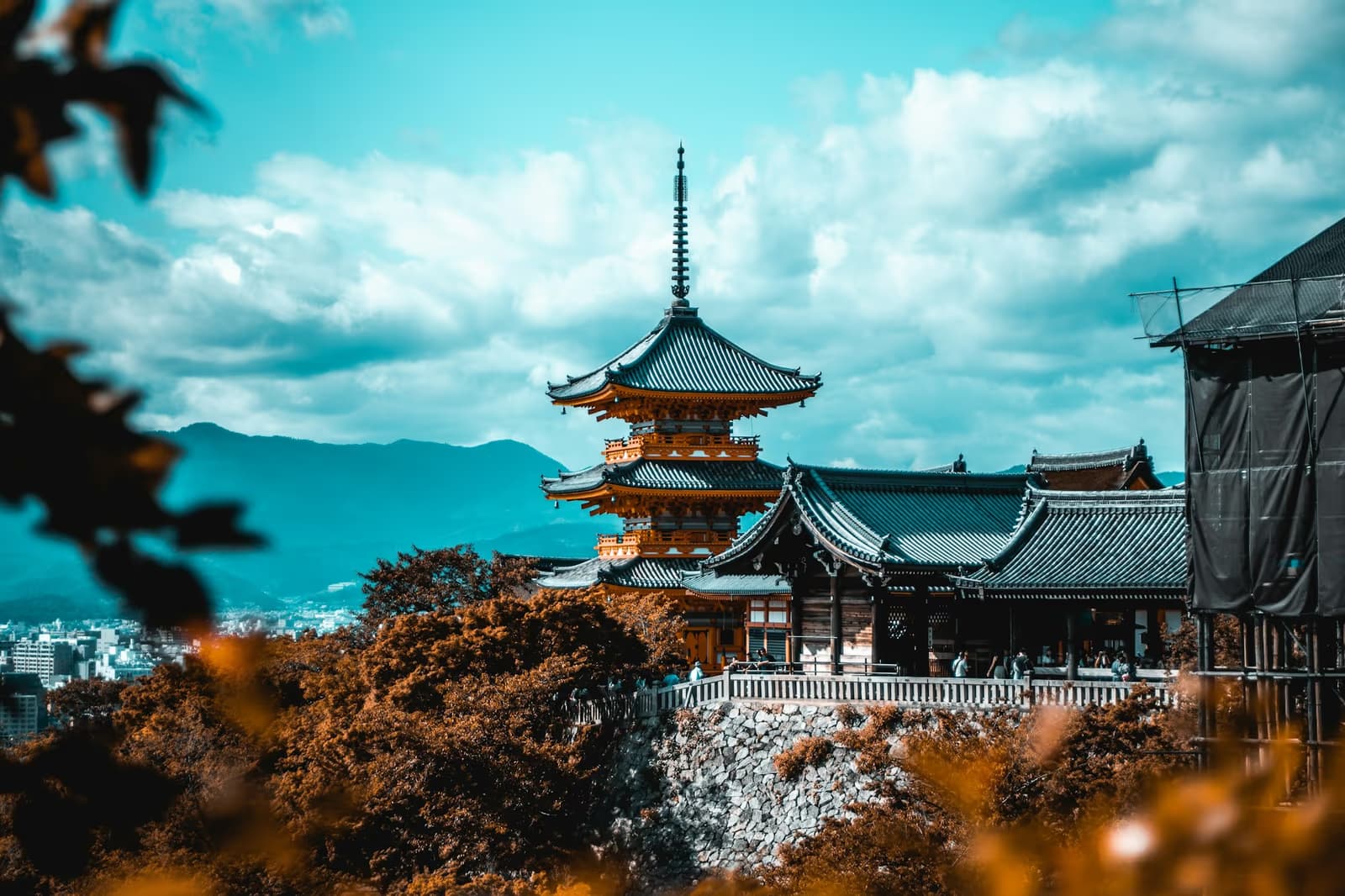 The three-storey pagoda and halls of Kiyomizu-dera above Kyoto, with autumn trees in front and mountains behind