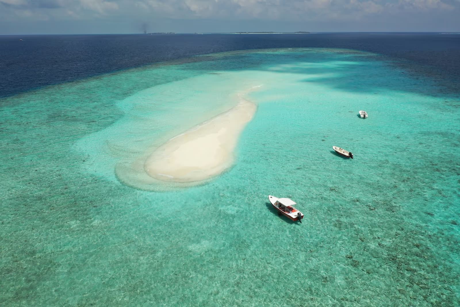 Three small boats anchored in a turquoise lagoon beside a white sandbank in the Maldives
