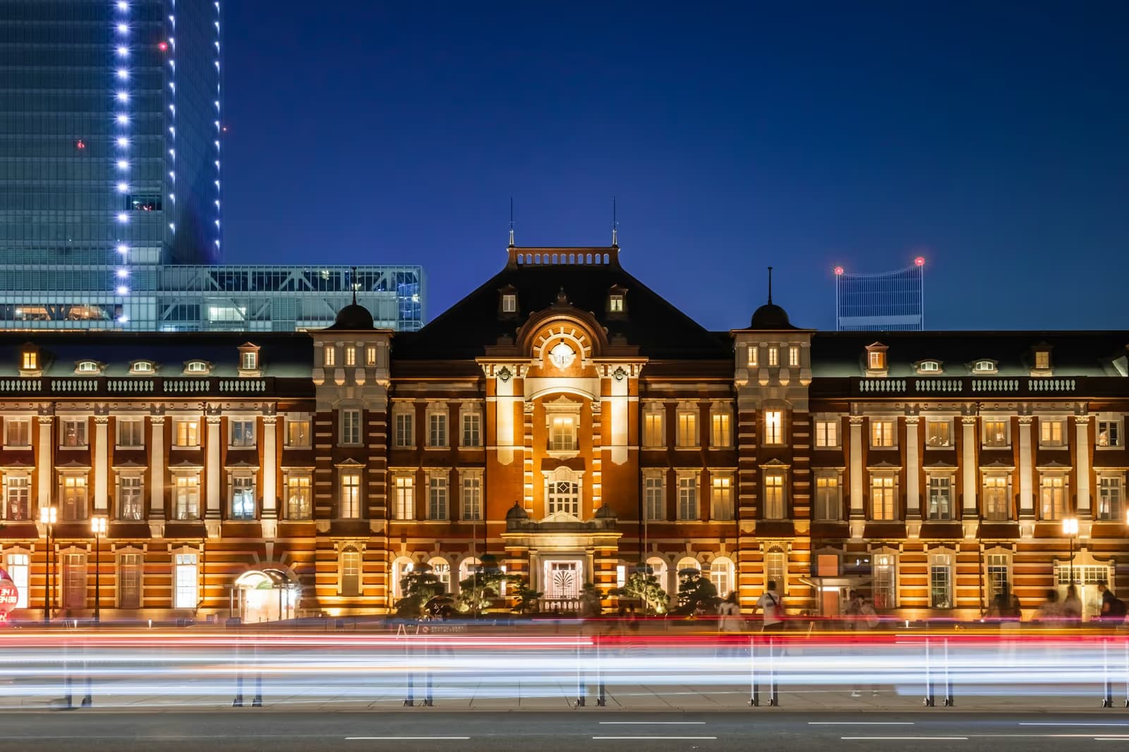 The red-brick Marunouchi building of Tokyo Station lit up at dusk, with light trails from passing cars