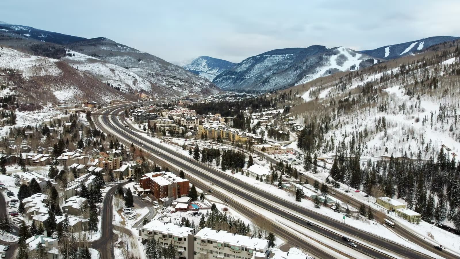 Aerial view of Vail in winter, with snow-covered mountains above the town and Interstate 70 running along the valley