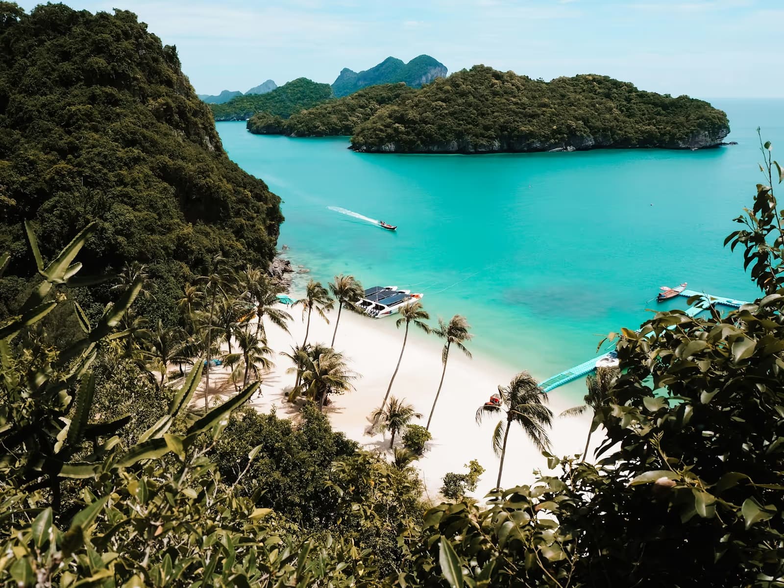 A white-sand beach lined with palms below forested limestone islands and turquoise water